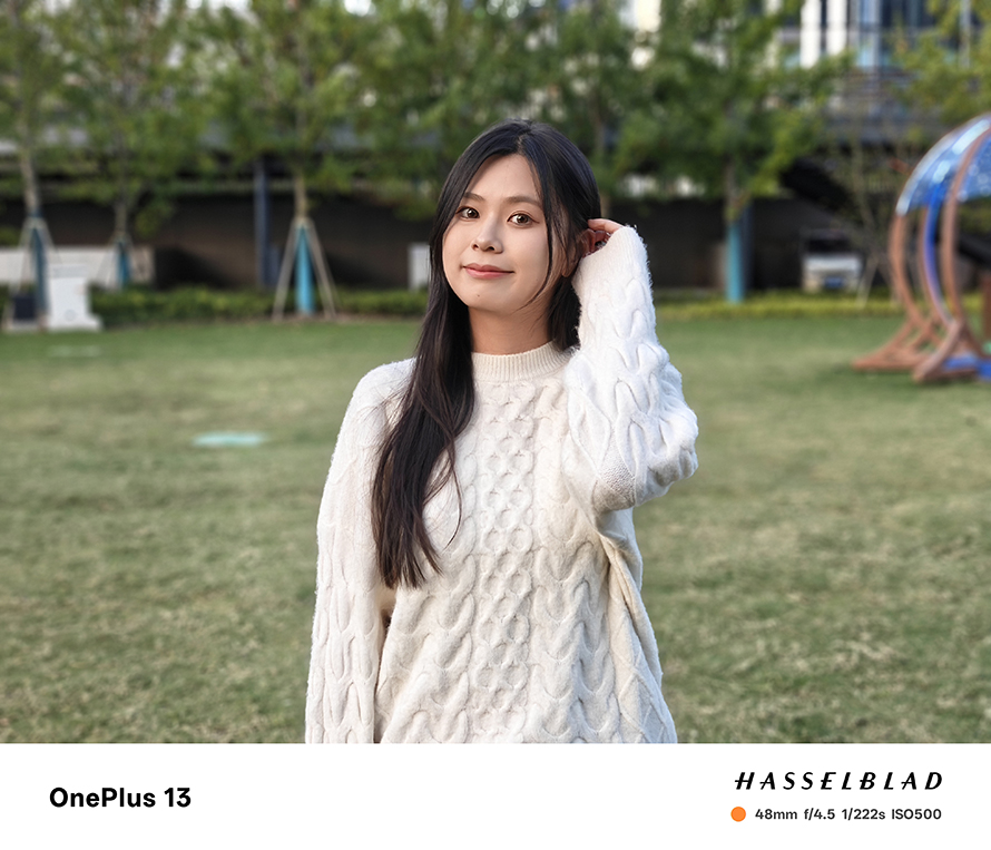 Outdoor portrait of a young woman in a grassy field, highlighting the OnePlus 13’s natural tones and bokeh effect.