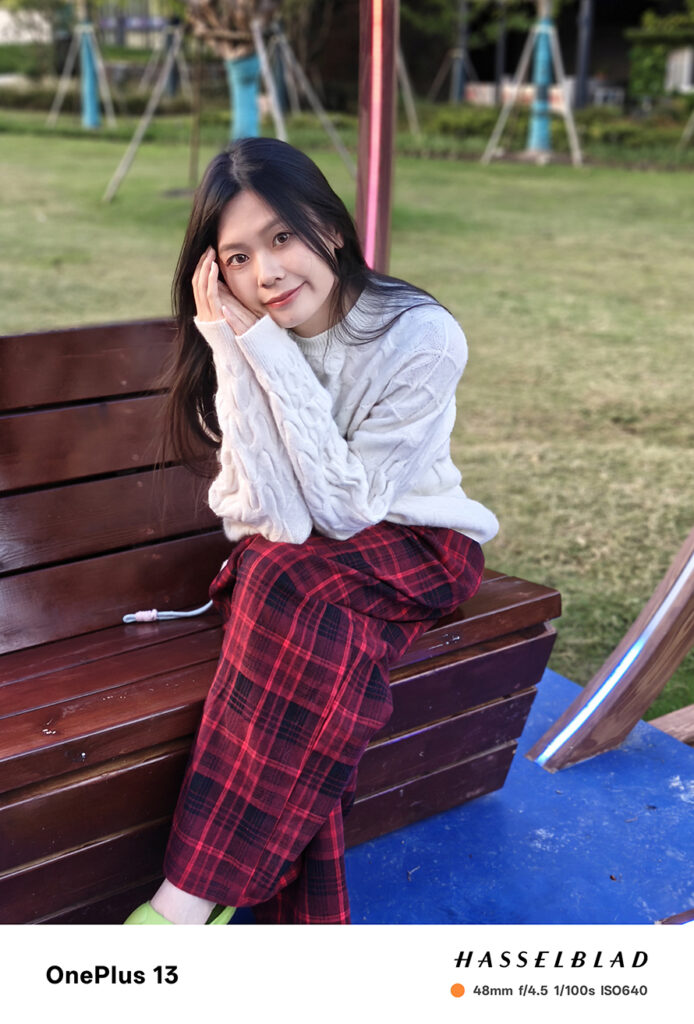 Portrait of a young woman sitting on a wooden bench, captured with the OnePlus 13, showcasing vibrant colors and clarity.