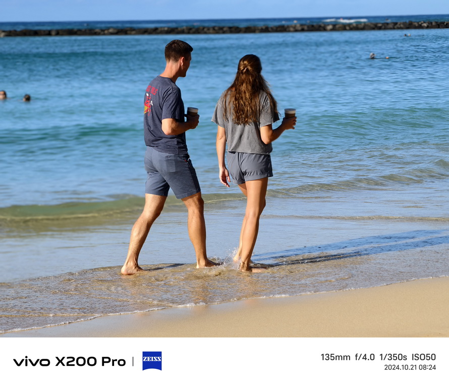 A couple walking along a serene beach, captured with the Vivo X200 Pro’s 135mm telephoto lens, showcasing vibrant colors and precise focus.