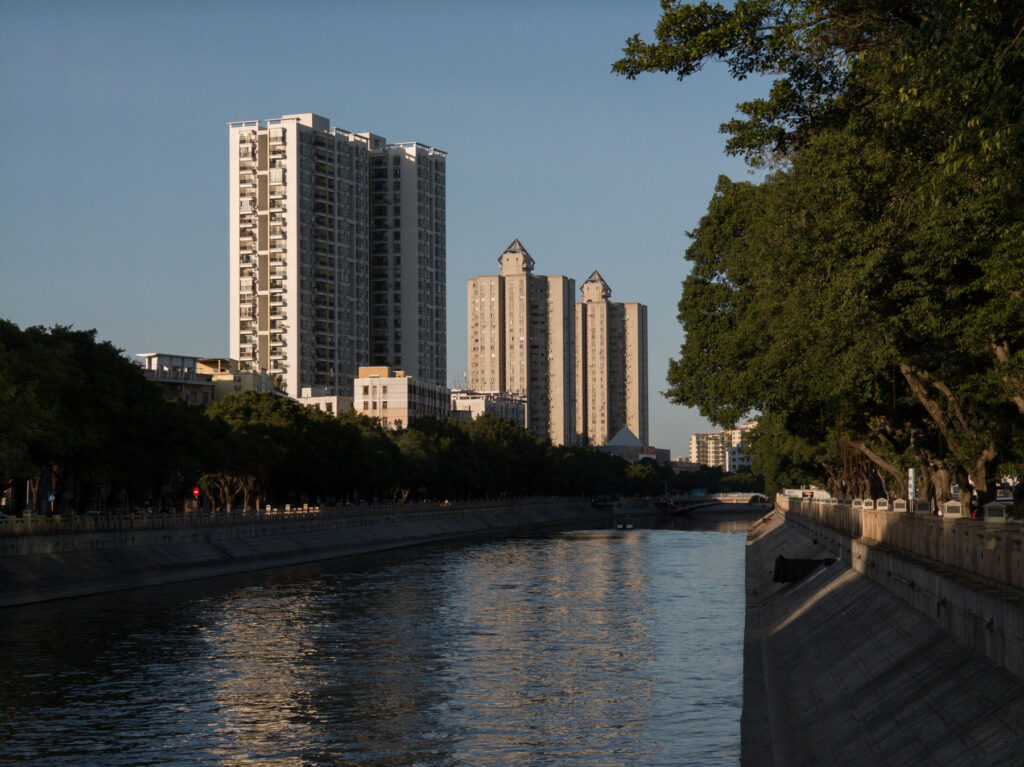 A scenic urban riverside view with tall buildings and greenery under natural daylight.