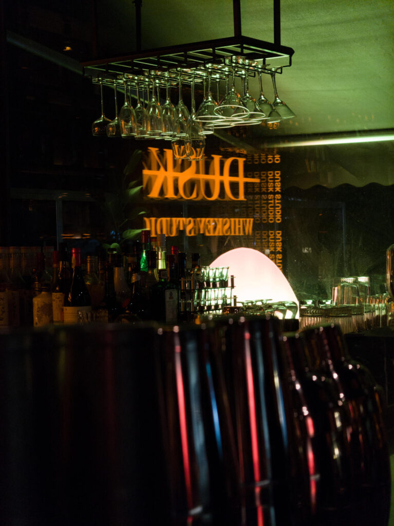 Indoor shot of a bar with a neon ‘Dusk’ sign, showcasing vibrant lighting and depth of detail.