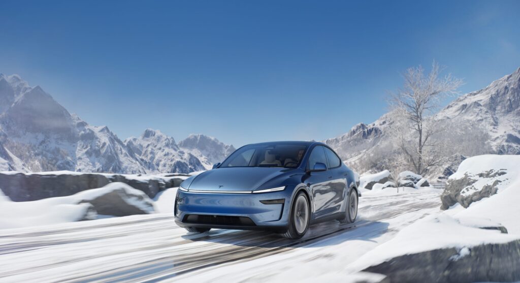 Tesla Model Y facelift driving through a snowy mountain landscape, showcasing its all-wheel-drive capabilities and winter performance.