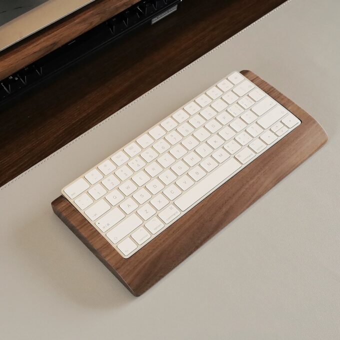 Close-up view of a Magic Keyboard on a wooden wrist rest tray, highlighting its sleek, ergonomic design and natural wood finish.