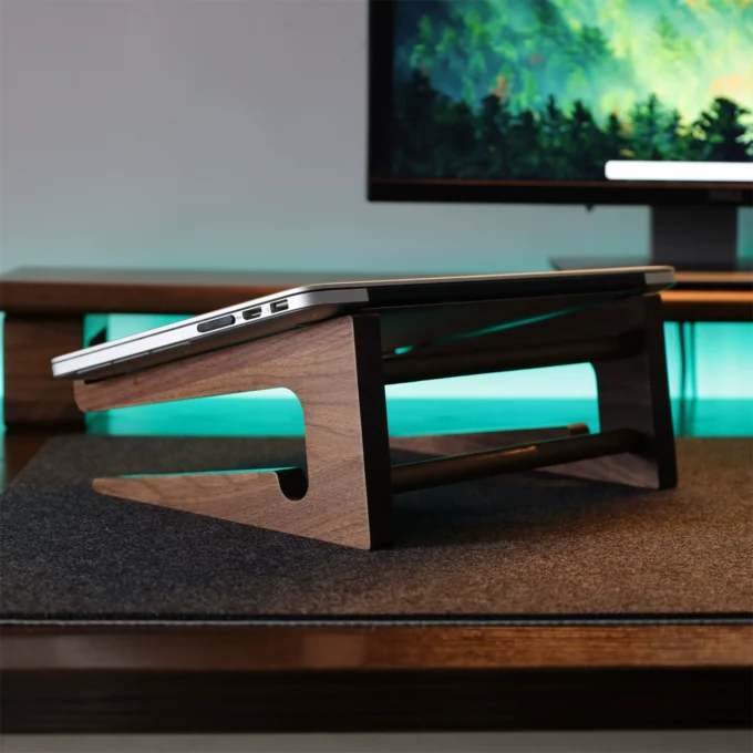 Side perspective of a MacBook on a walnut stand, elevating the screen above the desk for improved viewing.