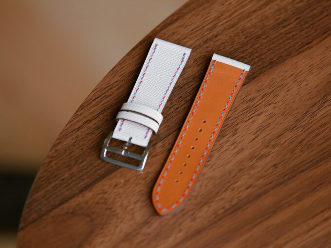 The white band showing its tan underside and silver buckle, highlighting the smooth French cowhide finish.