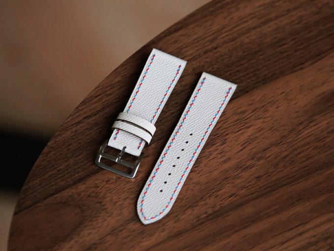 A close-up view of the two white leather watch band pieces side by side on a round wooden tabletop.