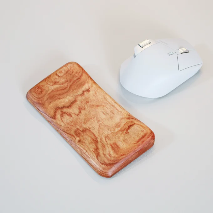 Top view of an Artisan Wood Ergonomic Mouse Wrist Rest with a swirled grain pattern, placed next to a white computer mouse on a white surface.