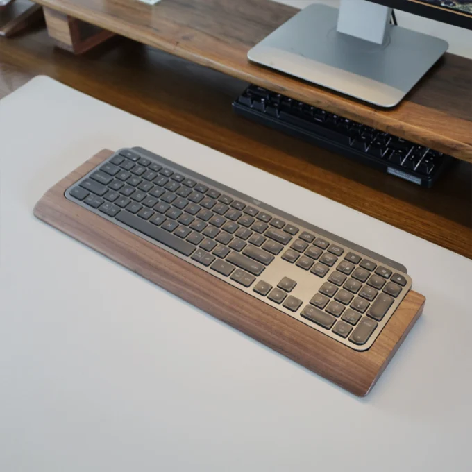 Slightly angled view of the Walnut Wood Wrist Rest Tray beneath a Logitech MX Keys keyboard, highlighting the contoured design and refined walnut surface.