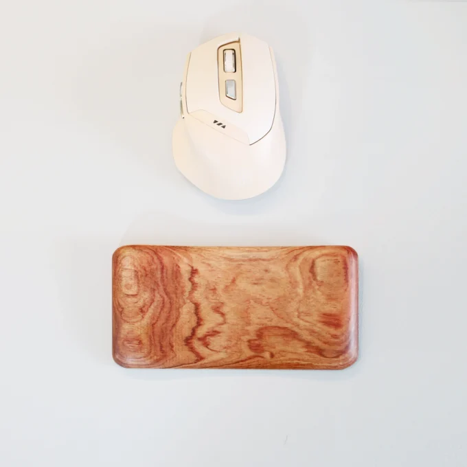 Overhead shot of an Artisan Wood Ergonomic Mouse Wrist Rest next to a white mouse, emphasizing its smooth rounded edges.