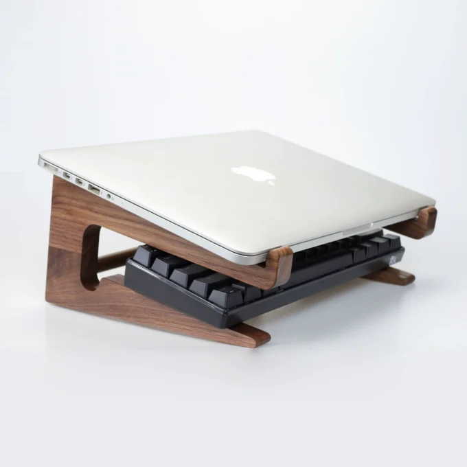 A MacBook raised on a walnut stand with space beneath for a keyboard, highlighting the stand’s dual-level design.