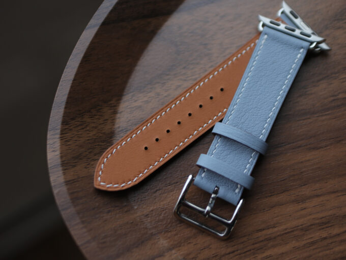 Top view of the watch band’s perforations and silver buckle against a warm wood background.