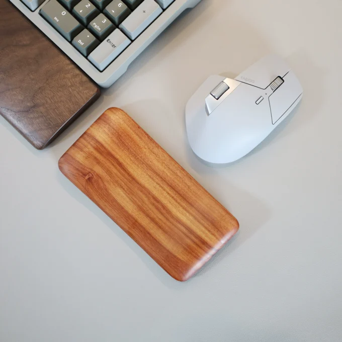 The Artisan Wood Ergonomic Mouse Wrist Rest alongside a keyboard and white mouse, showing how it fits in a typical desktop setup.