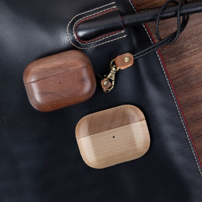 A pair of walnut and maple wood AirPods cases, each with an attached leather strap, highlighting their minimalist design.