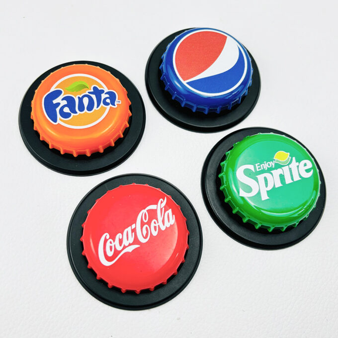 Four bottle cap grips featuring Fanta, Coca-Cola, Pepsi, and Sprite logos, laid out on a white surface with black stands.