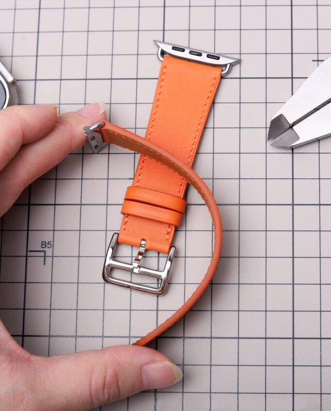 Person holding a bright orange French Swift Leather Apple Watch band, demonstrating its softness and flexible grain.