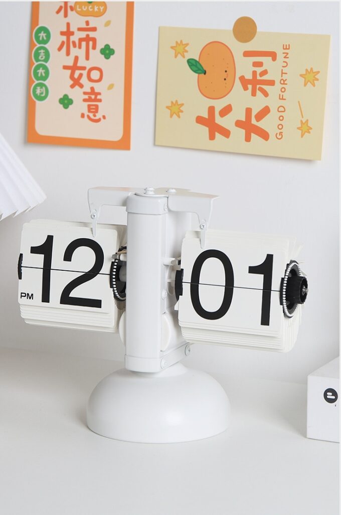 A silent mechanical flip desk clock displaying “12:01 PM,” positioned in a stylish space with colorful wall decor.