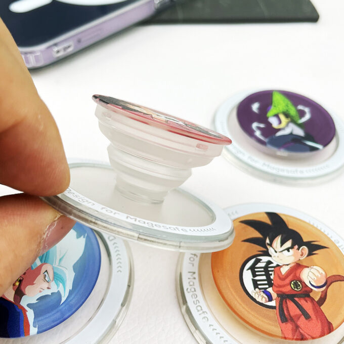 A partially extended grip demonstrating its foldable stand feature, surrounded by additional Goku-themed designs on a table.