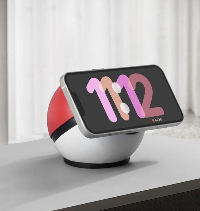 The same spherical charger holding a phone in landscape mode, displaying a digital clock reading “11:12.”