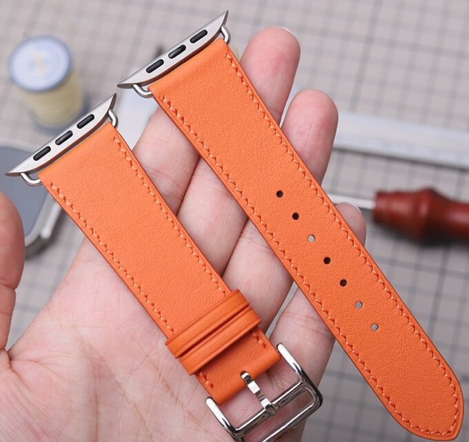 Person holding a bright orange French Swift Leather Apple Watch band, demonstrating its softness and flexible grain.