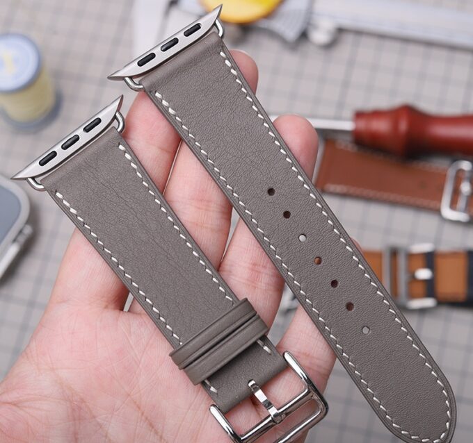 Close-up of a gray Apple Watch band crafted from French Swift Leather, featuring a stainless steel buckle and adapters.