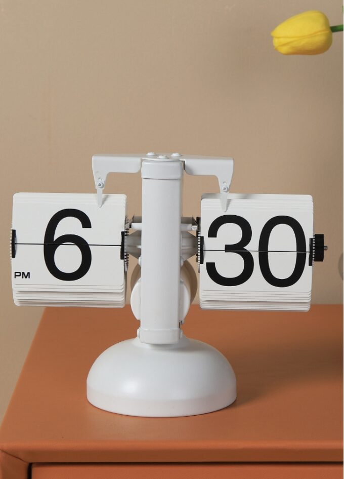 A retro flip clock with a white frame and bold black numerals, placed on a beige surface for a cozy, vintage feel.