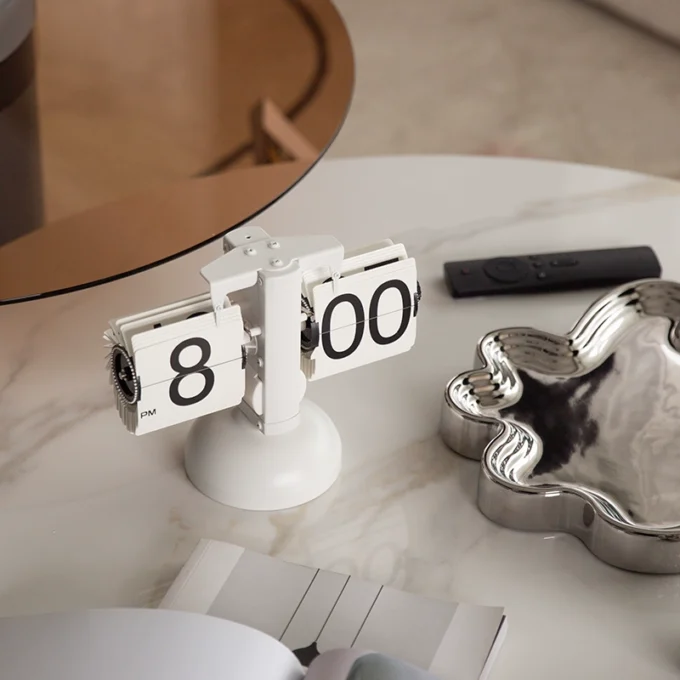 A white retro flip desk clock placed on a marble table, accompanied by decorative elements for an elegant touch.