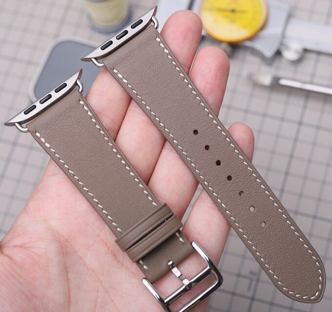 A gray French Swift Leather Apple Watch band, featured in someone’s hand to highlight the refined stitching and hypoallergenic stainless steel buckle.