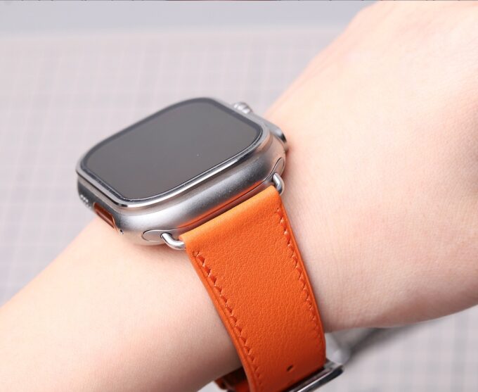 Close-up of an Apple Watch on a wrist featuring an orange French Swift Leather band, highlighting the comfortable fit and smooth finish.