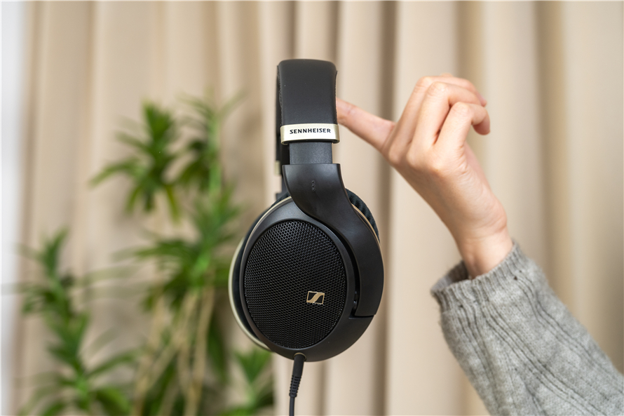 Hand holding Sennheiser HD 505 headphones with open-back ear cups, highlighting the minimalist design and natural soundstage in a cozy indoor setting with a plant in the background.